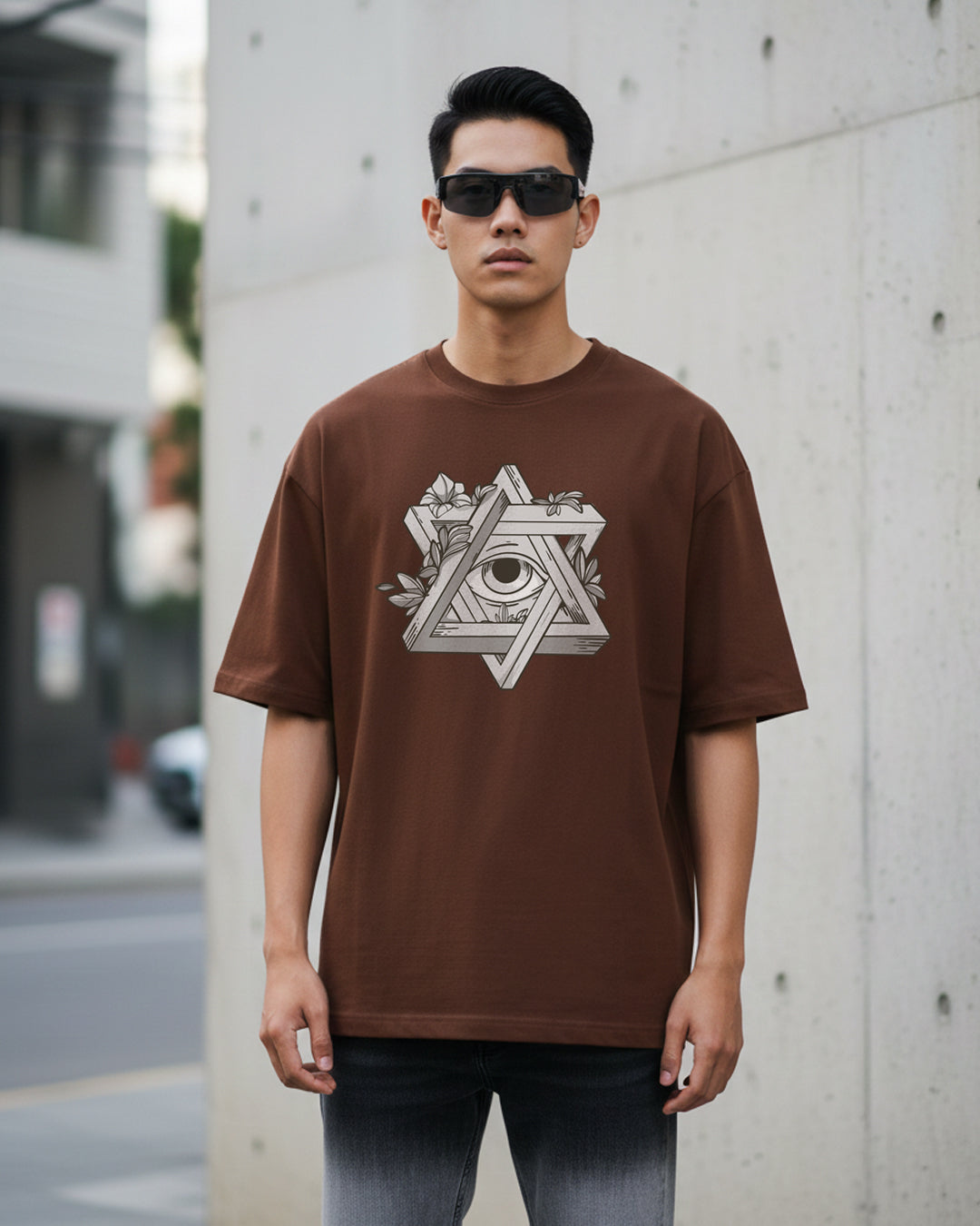 Front view of a man wearing 'The Futurist' oversized coffee brown t-shirt featuring a white and grey geometric star graphic with an eye in the center and leaf accents.