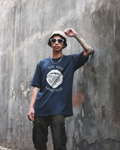 Front view of a navy blue oversized t-shirt featuring a large white graphic of a mouth with tabs on the tongue and the text 'THE KIDS WANT ACID' in a hand-drawn style.