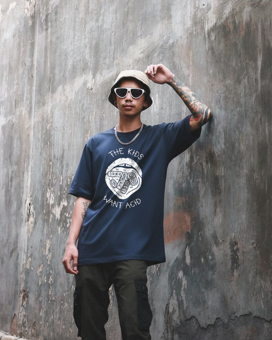 Front view of a navy blue oversized t-shirt featuring a large white graphic of a mouth with tabs on the tongue and the text 'THE KIDS WANT ACID' in a hand-drawn style.